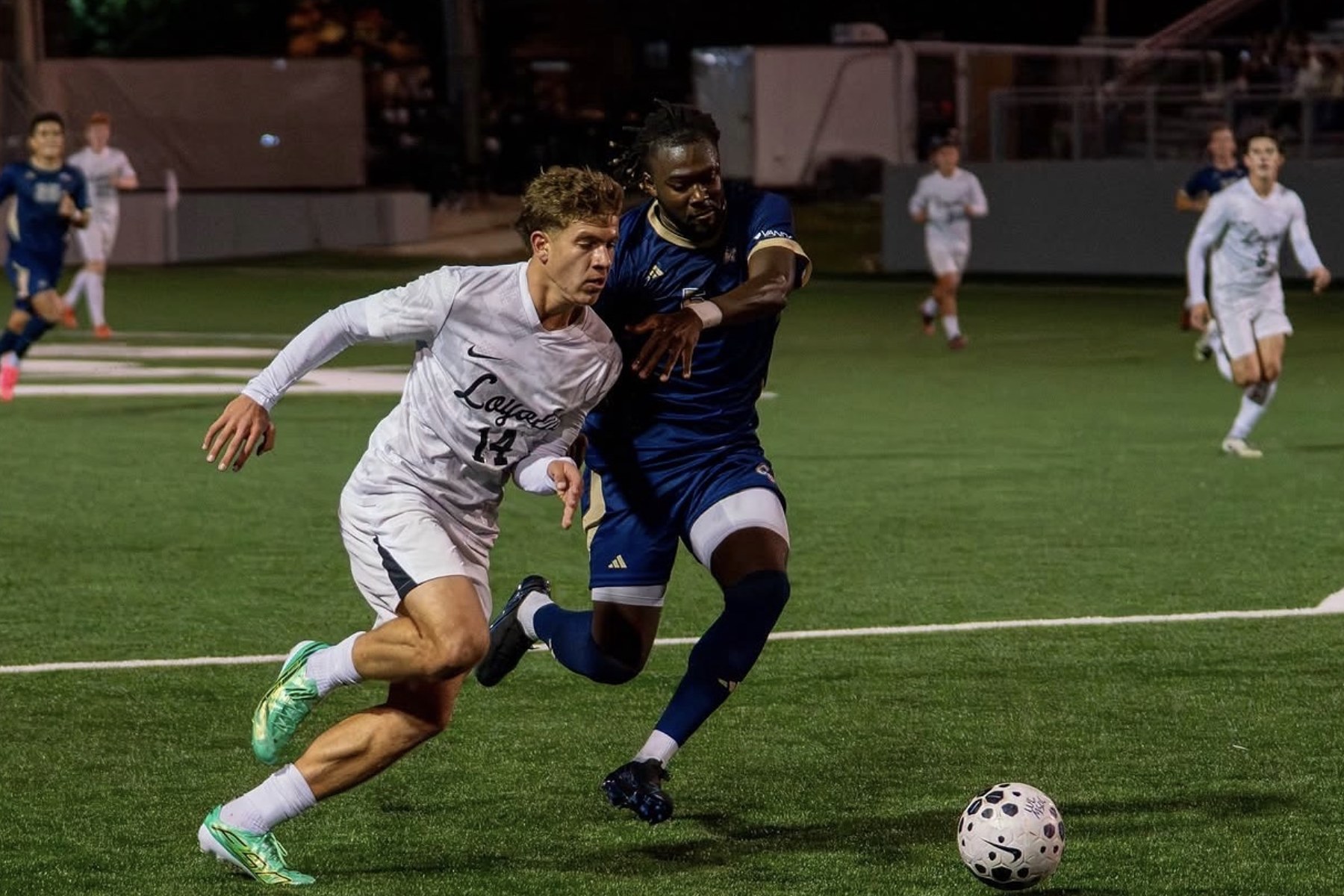 A soccer player in white driving past a defender with the ball at his feet, under the lights