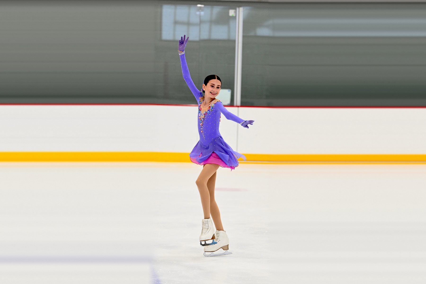 A young figure skater smiling mid-program, one arm raised